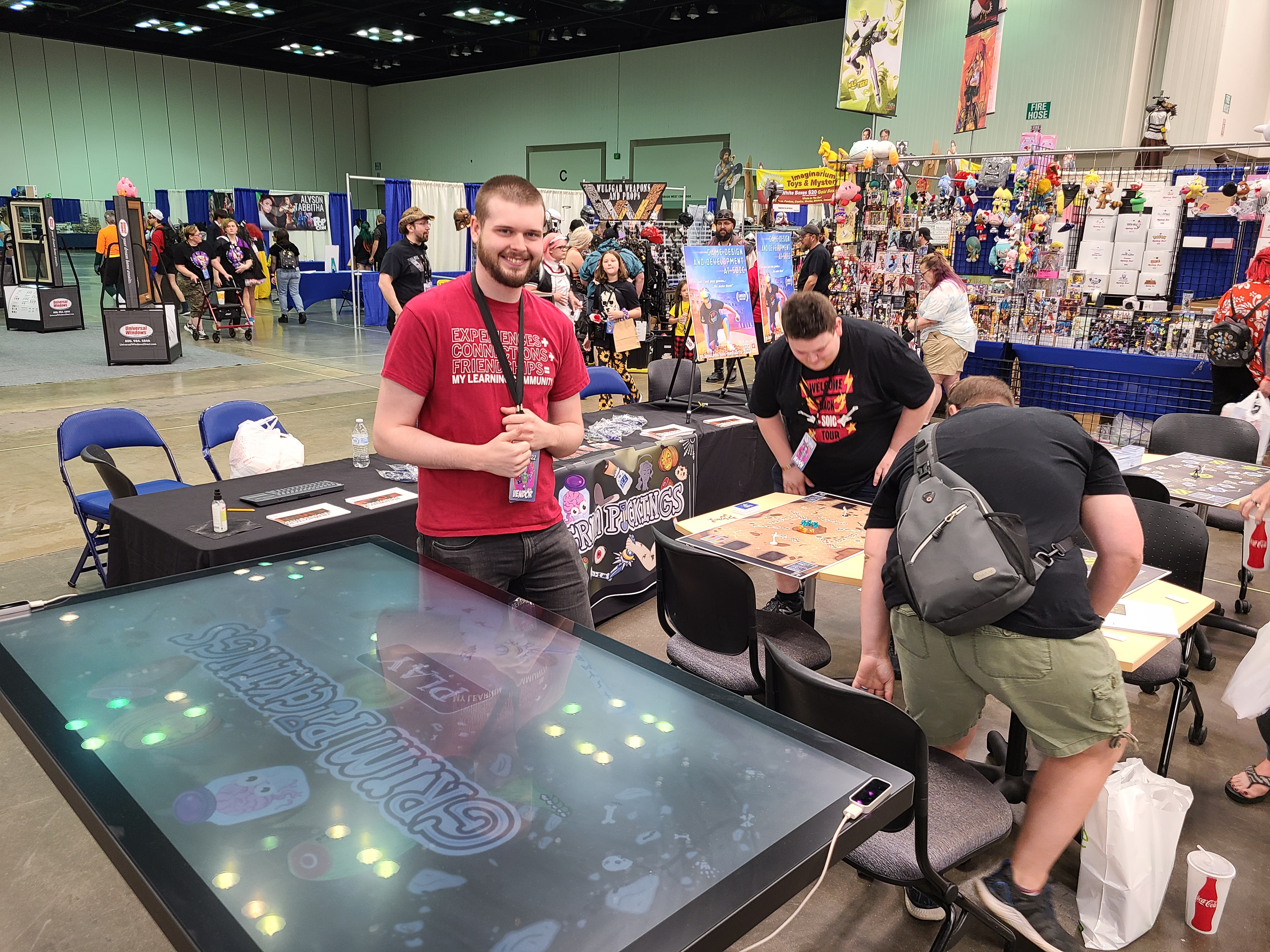 jake oaks, software developer posing with the IQ table where he ported the tabletop game Grim Pickings to PC
